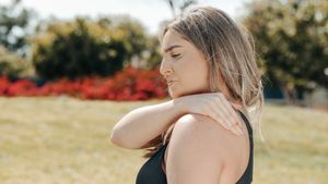 Woman in black tank top touching shoulder outdoors. Concept of shoulder pain and relaxation.